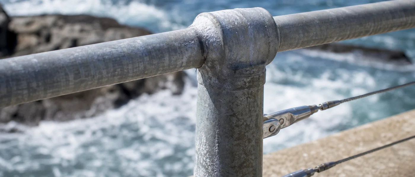 Galvanized handrail and stainless fixings on a coastal walkway with salt residue